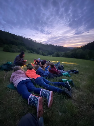 Kindeer liegen bäuchlinks bei Abenddämmerung auf einer Wiese und lauschen dem Erzähler
